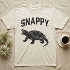 Snapping Turtle Snappy T-Shirt in Natural — Worn one-ink print of a common snapping turtle crouched side-on, jaws open mid-snap, under the arched word SNAPPY