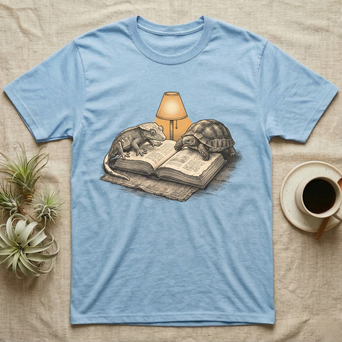 Cold-Blooded Book Club T-Shirt in Light Blue — Engraved cozy illustration of a gecko and a tortoise sharing an open book under a glowing reading lamp.