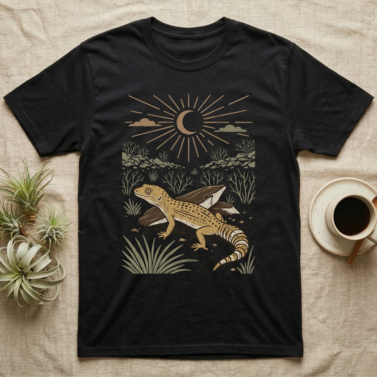 Leopard Gecko Home Range T-Shirt in Black — Woodcut-style illustration of a leopard gecko standing on cracked earth beside flat stones with thorn scrub behind, no on-shirt text.