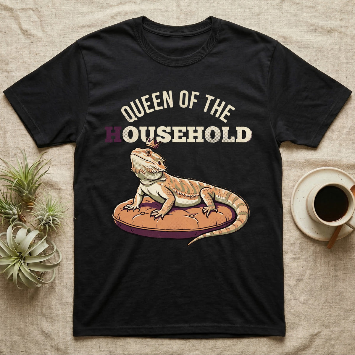 Queen Bearded Dragon T-Shirt in Black — Bold-vector illustration of a bearded dragon on a throne-cushion with a crown under varsity Queen of the Household lettering.