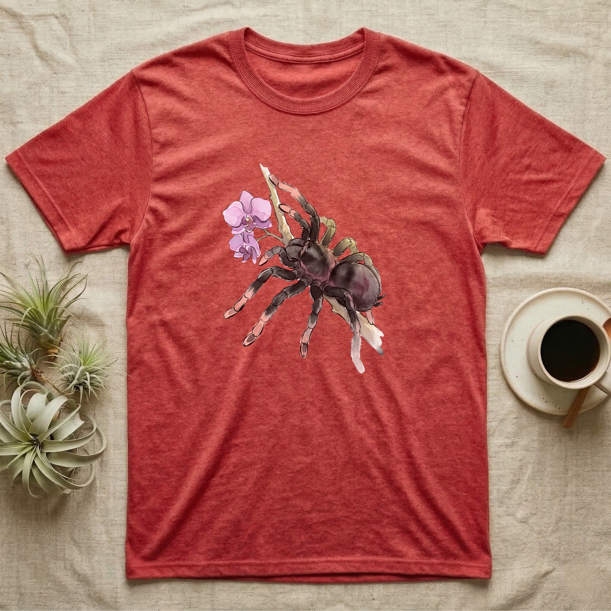 Pink-Toe Tarantula Blossom T-Shirt in Heather Red — Watercolor illustration of a charcoal pink-toe tarantula with salmon toe tips holding an orchid blossom sprig, on a dark grey t-shirt.
