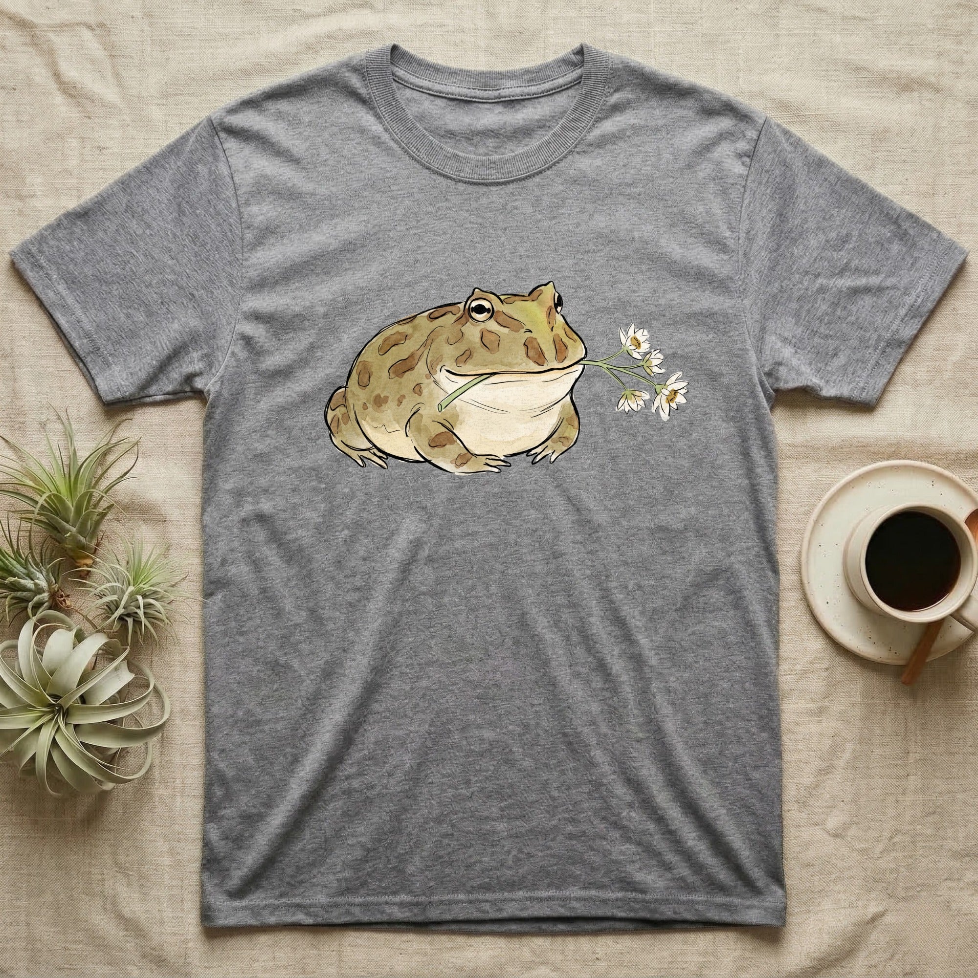 Pacman Frog Blossom T-Shirt in Sport Grey — Watercolor illustration of an olive-tan Pacman frog holding a water-lily blossom sprig, on a dark grey t-shirt.