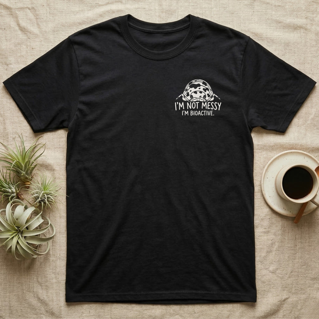 Bioactive Dairy Cow T-Shirt in Black — White dairy cow isopod with black cow patches peeking over white marker capitals reading I'M NOT MESSY I'M BIOACTIVE.