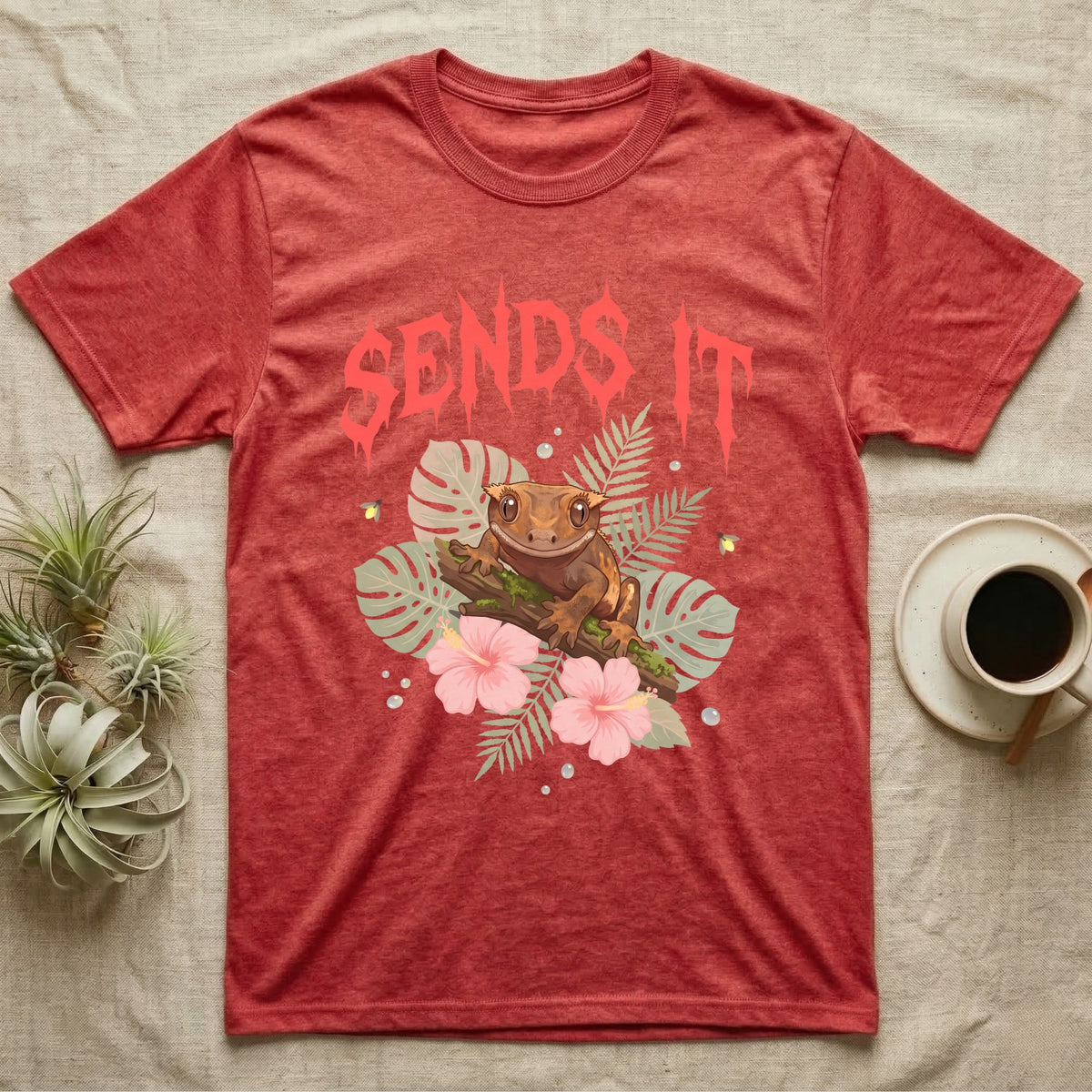 Crested Gecko Feral T-Shirt in Heather Red — Crested gecko on a mossy branch in a pastel jungle scene under a spiky coral metal wordmark reading SENDS IT.