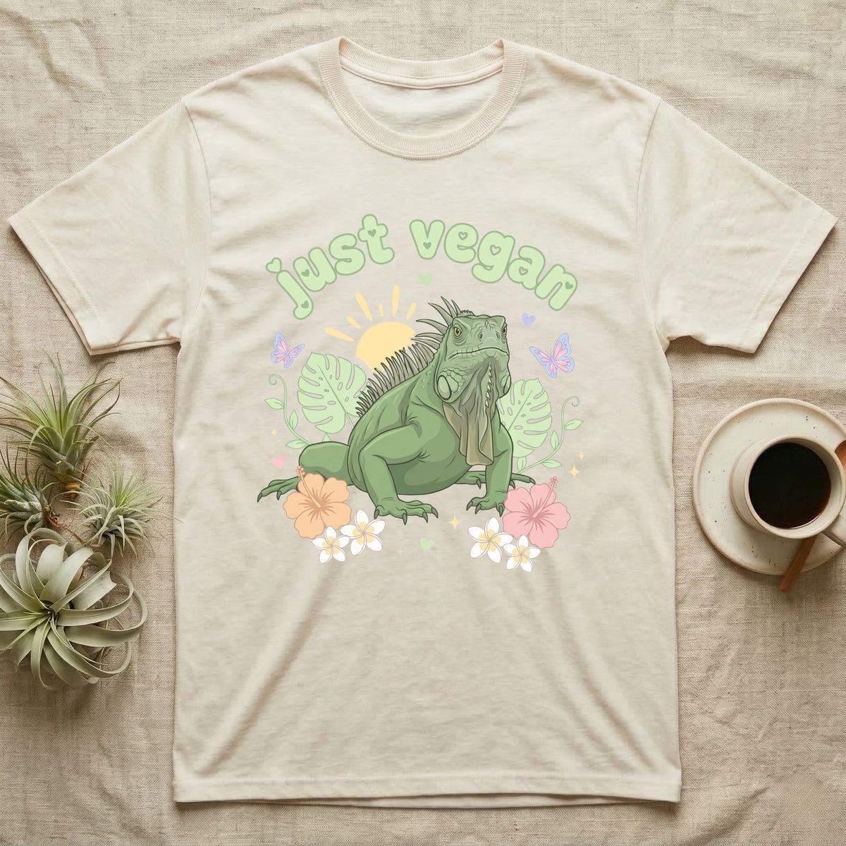 Green Iguana Baby T-Shirt in Natural — Green iguana with spiky crest and dewlap among pastel leaves and flowers under puffy green bubble text "just vegan".
