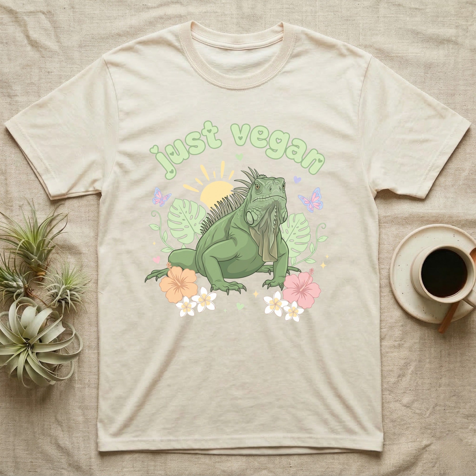 Green Iguana Baby T-Shirt in Natural — Green iguana with spiky crest and dewlap among pastel leaves and flowers under puffy green bubble text "just vegan".
