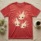 Vintage comic screen-print illustration of three axolotls clustered together with coral feathery gills and sparkling star-highlighted eyes, graphic-only, no text. — shown on a Heather Red tee.