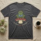 Dark grey t-shirt with a frog on a mushroom and the text "Let me be weird in peace."