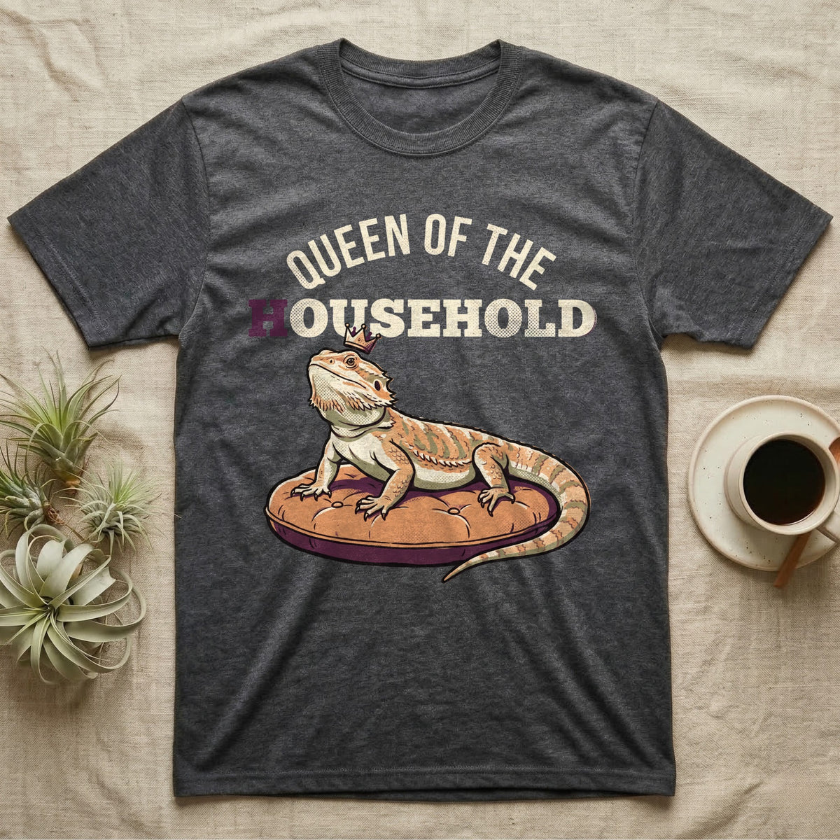 Queen Bearded Dragon T-Shirt in Dark Heather — Bold-vector illustration of a bearded dragon on a throne-cushion with a crown under varsity Queen of the Household lettering.